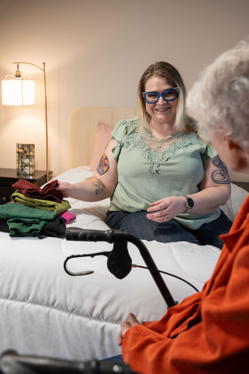 A smiling caregiver helps an elderly woman with laundry and home care services.