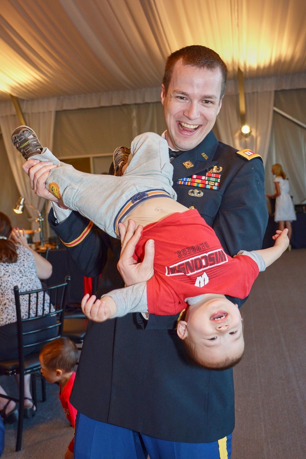 a man in military uniform holding a baby boy upside down in his arms