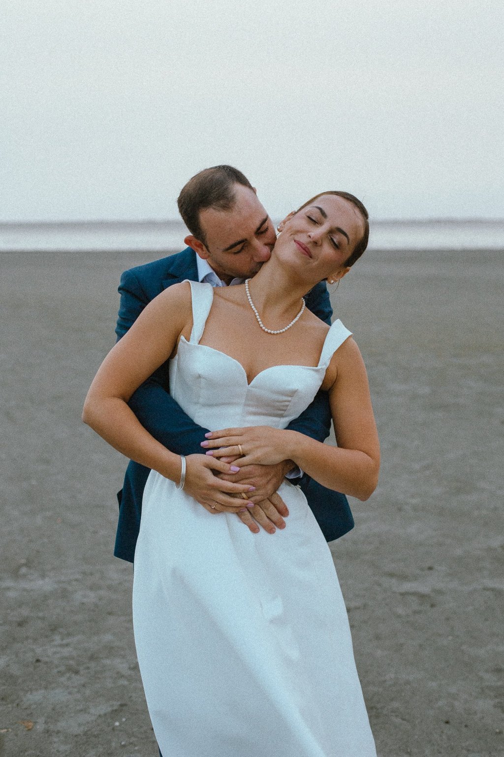 un marié qui embrasse sa femme dans le cou sur la plage