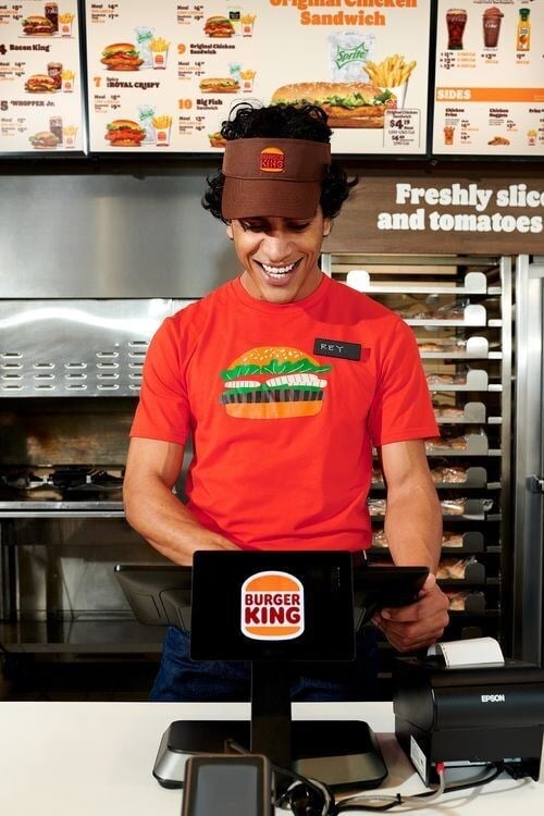 Smiling Burger King employee in a red t-shirt working at the fast food restaurant counter.