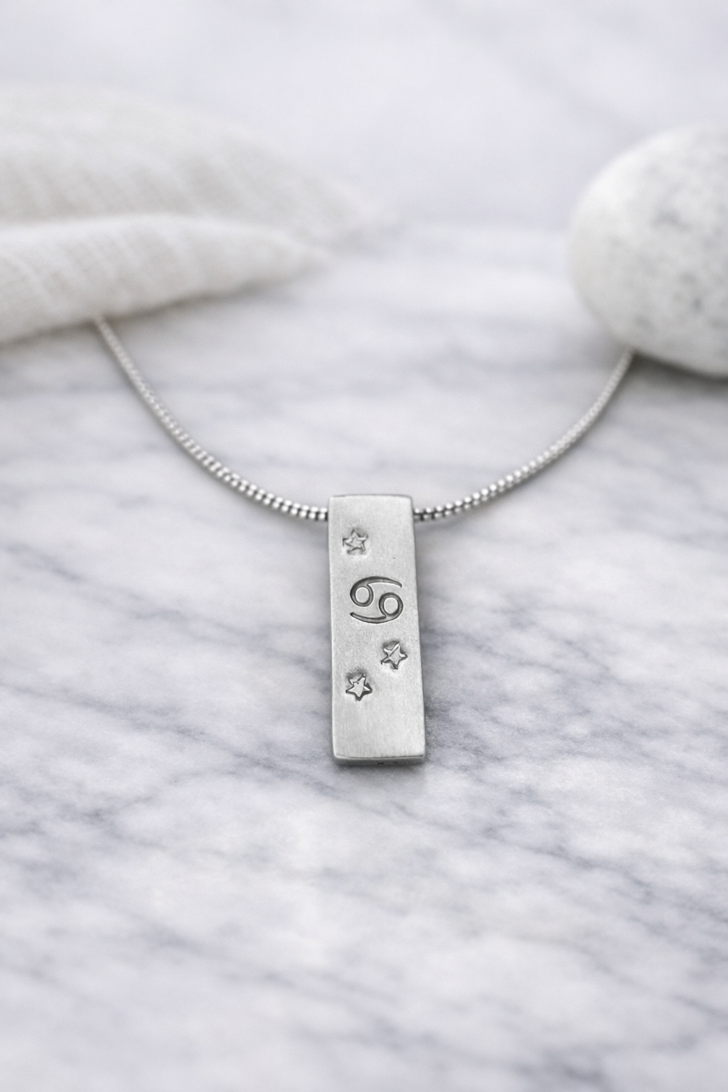 Handmade 999 silver Cancer zodiac necklace with a vertical bar pendant on a marble surface.