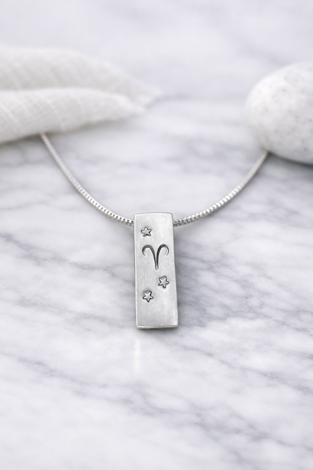 Handmade 999 silver Aries zodiac necklace with a vertical bar pendant on a marble surface.