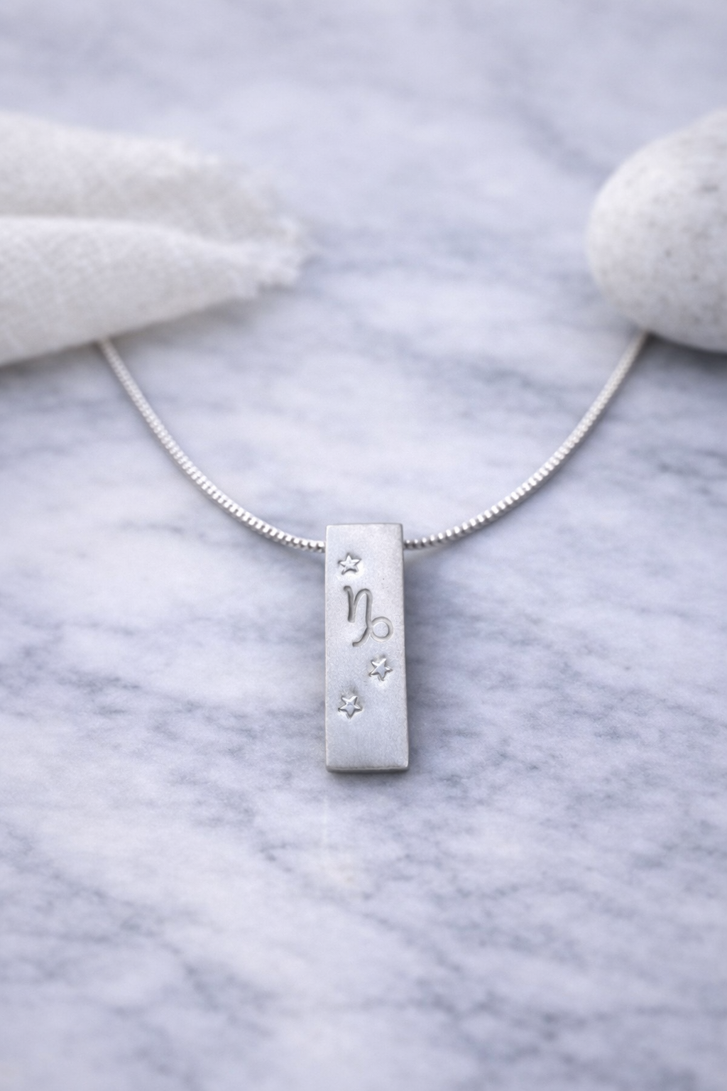 Handmade 999 silver Capricorn zodiac necklace with a vertical bar pendant on a marble surface.