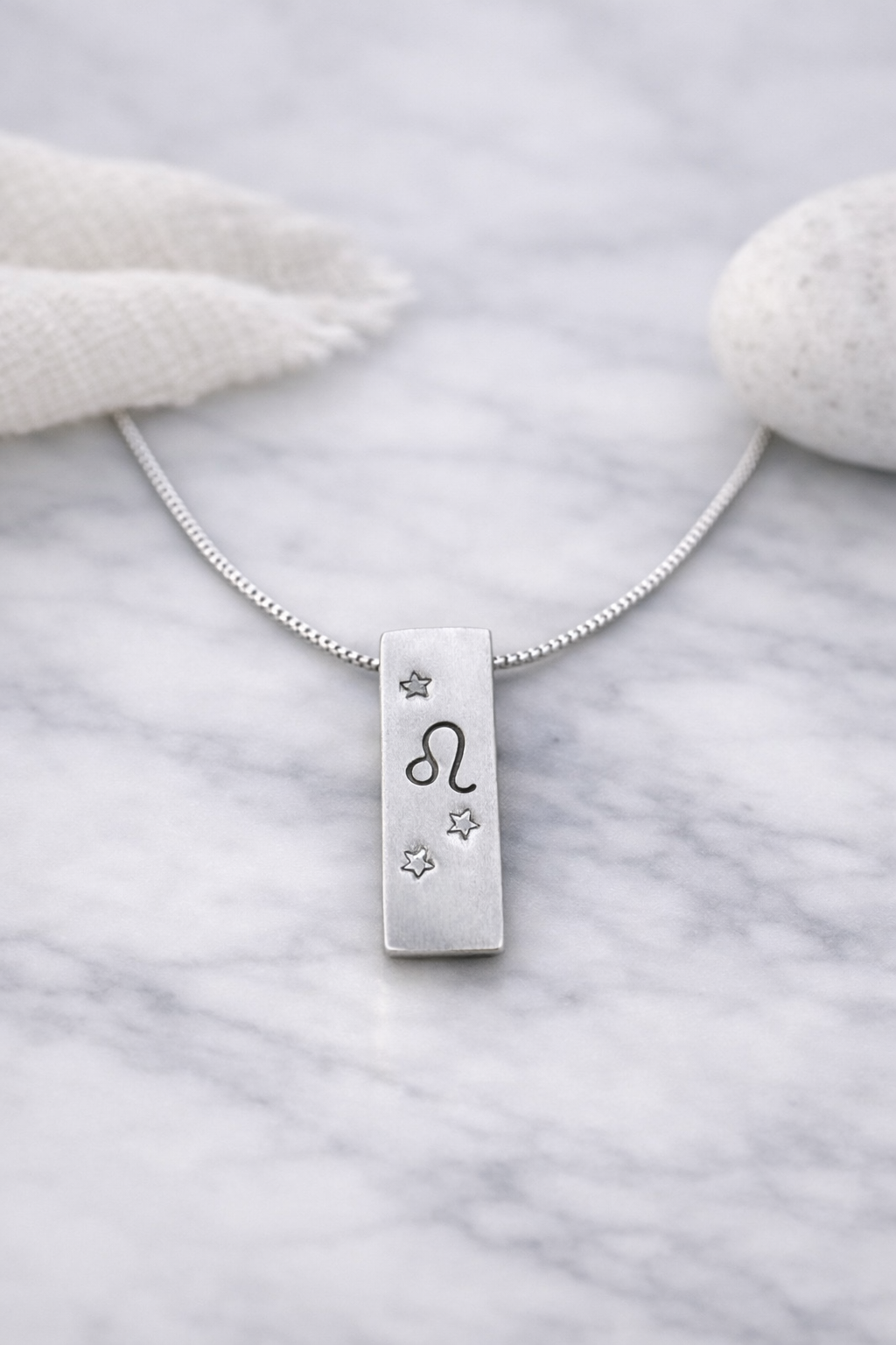 Handmade 999 silver Leo zodiac necklace with a vertical bar pendant on a marble surface.