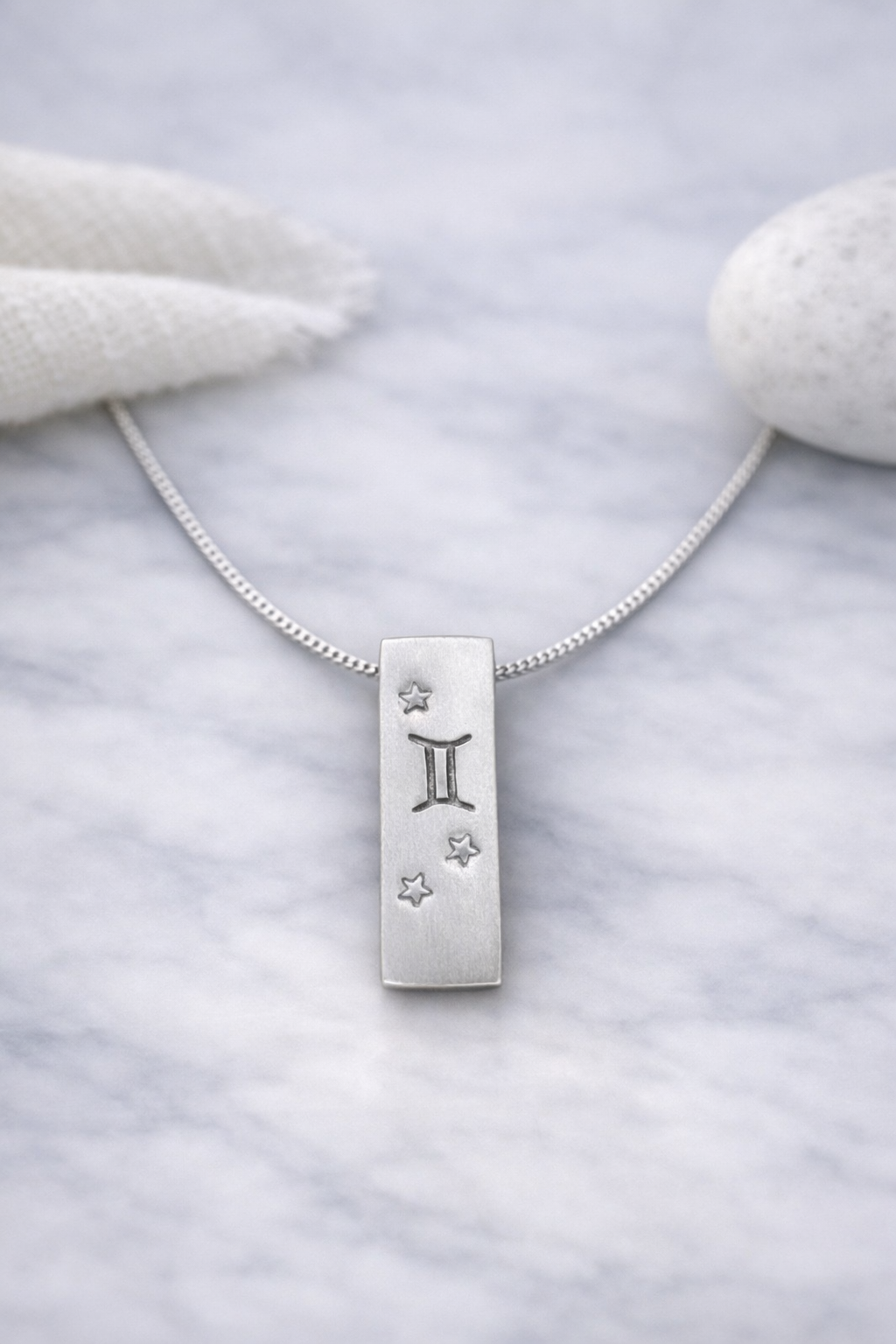 Handmade 999 silver Gemini zodiac necklace with a vertical bar pendant on a marble surface.