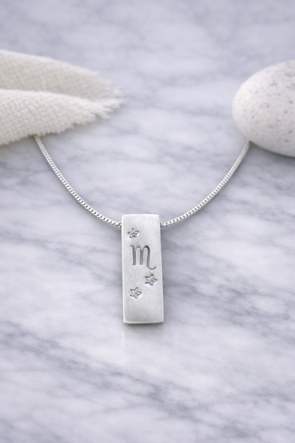 Handmade 999 silver Scorpio zodiac necklace with a vertical bar pendant on a marble surface.