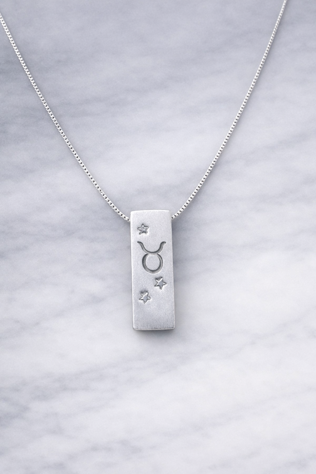 Handmade 999 silver Taurus zodiac necklace with a vertical bar pendant on a marble surface.