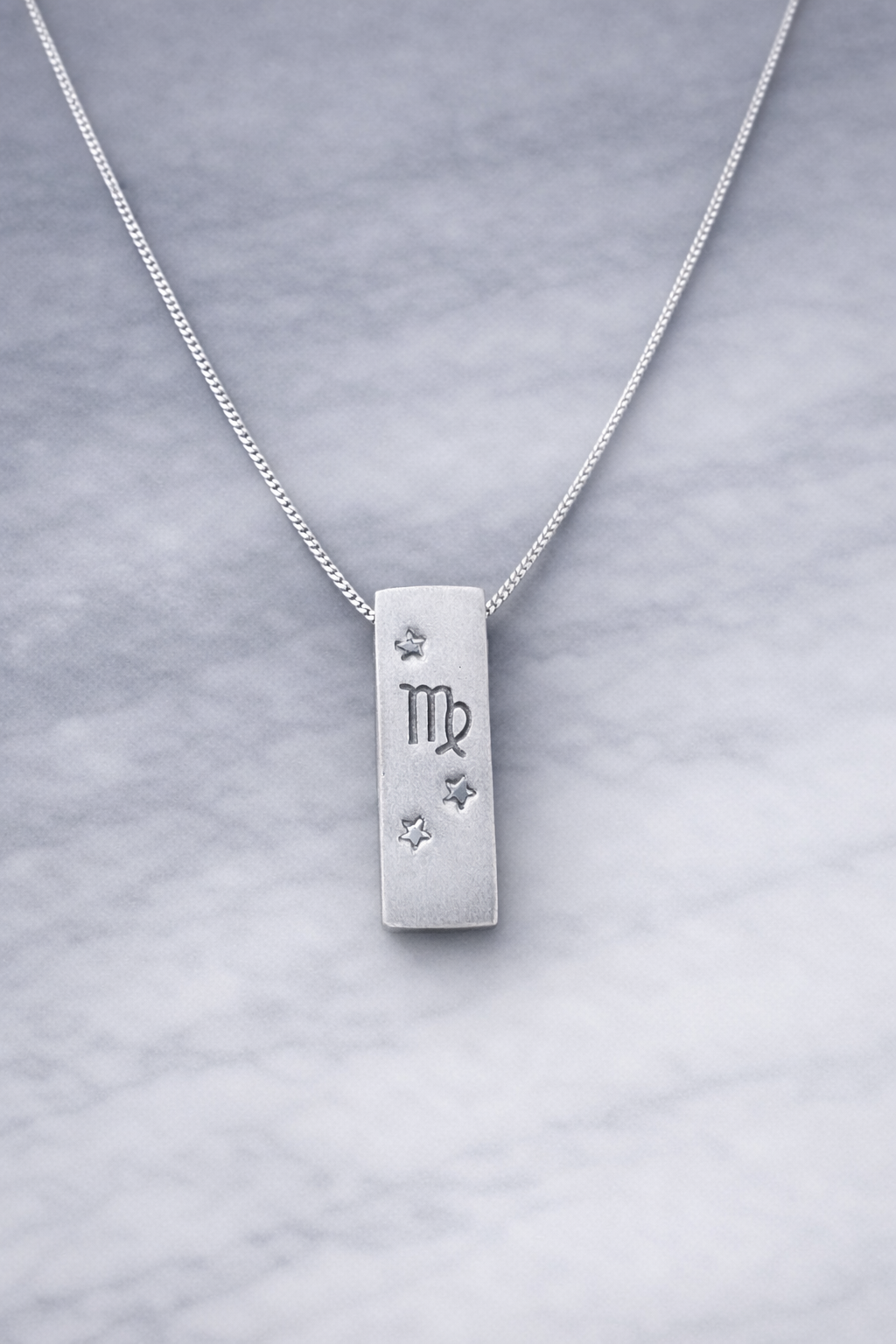 Handmade 999 silver Virgo zodiac necklace with a vertical bar pendant on a marble surface.