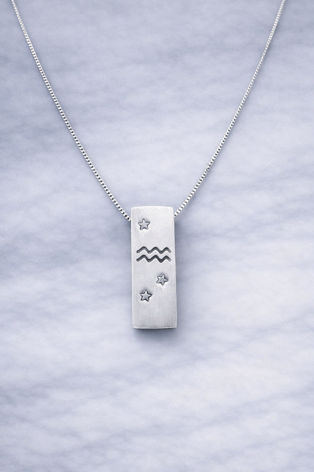 Handmade 999 silver Aquarius zodiac necklace with a vertical bar pendant on a marble surface.