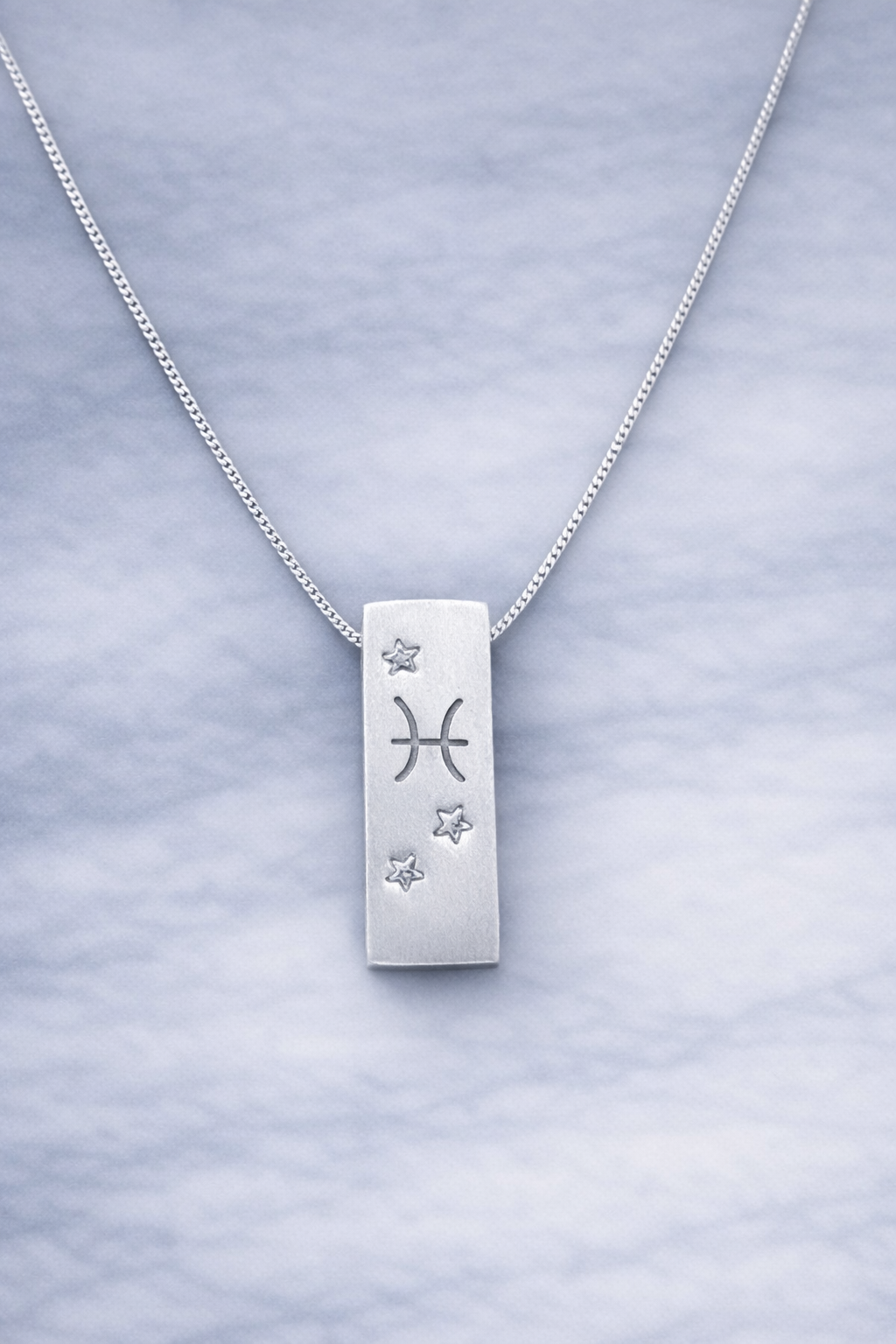 Handmade 999 silver Pisces zodiac necklace with a vertical bar pendant on a marble surface.