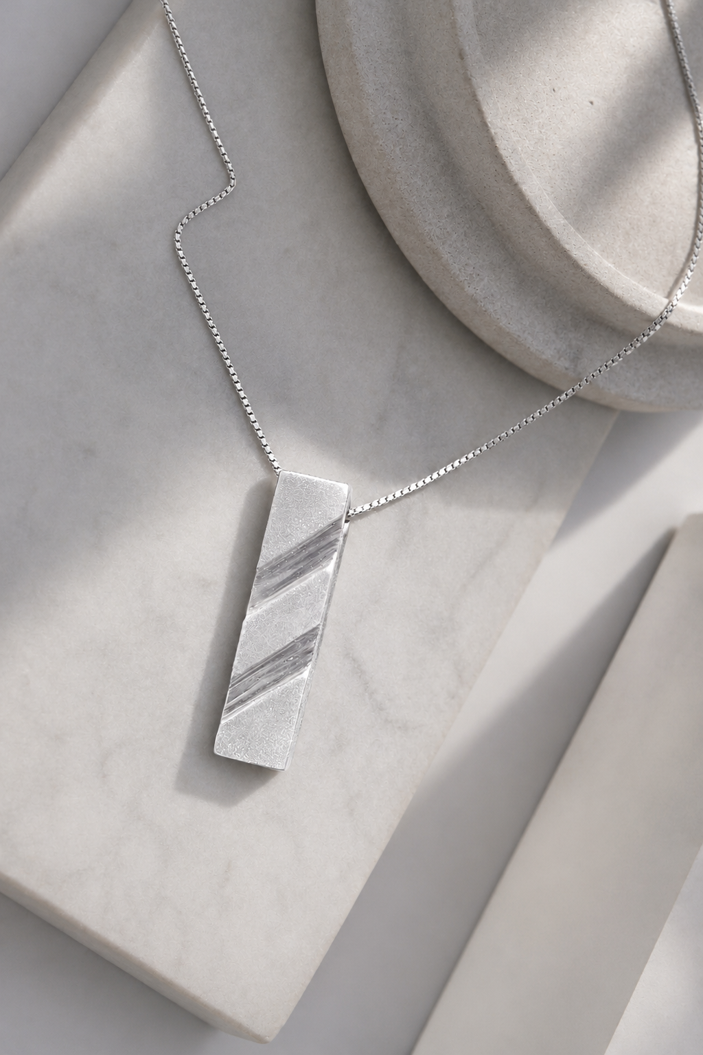 Handcrafted modern 999 fine silver pendant necklace displayed on a white marble surface.