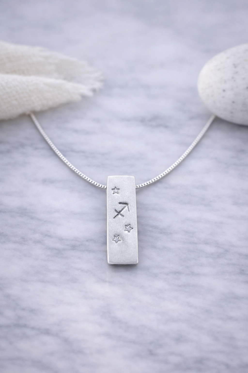 Handmade 999 silver Sagittarius zodiac necklace with a vertical bar pendant on a marble surface.