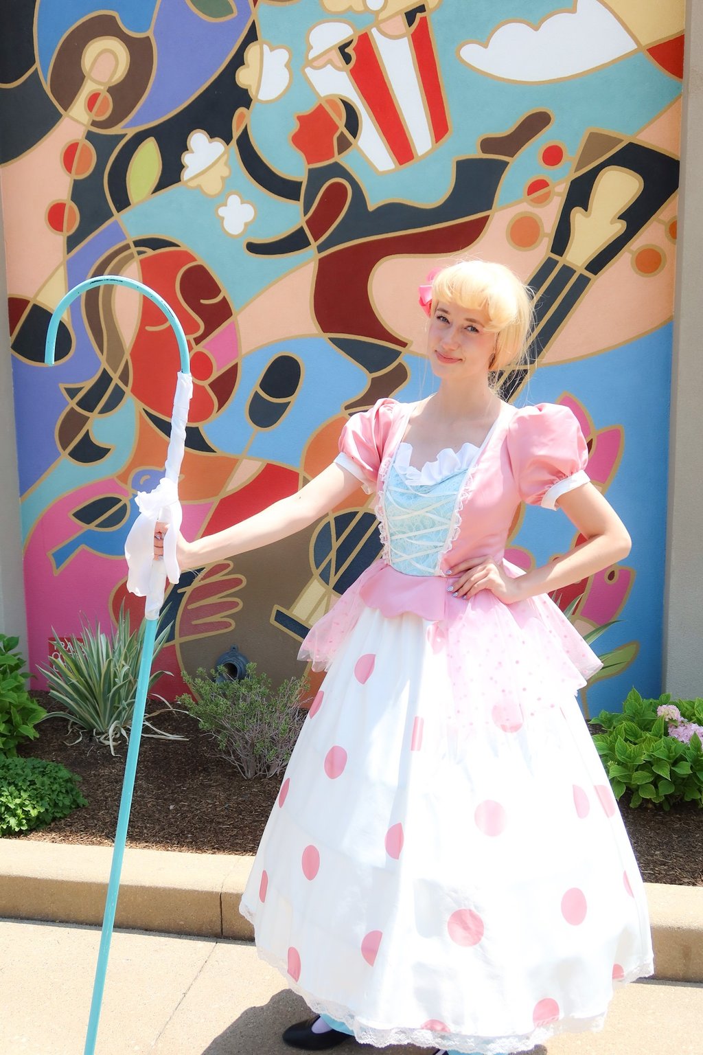 A beautiful girl with a blue shepherd's crook standing against a colorful mural.