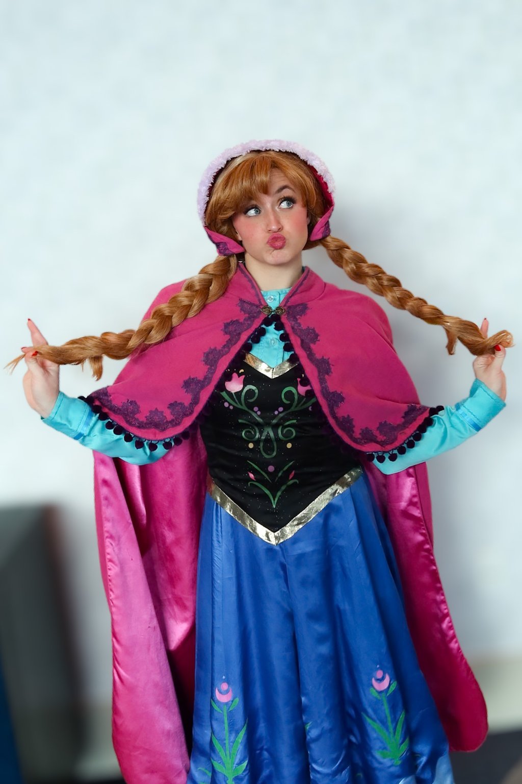 A cosplayer dressed as Princess Anna from Frozen wearing a pink cape and braided wig while making a funny face.