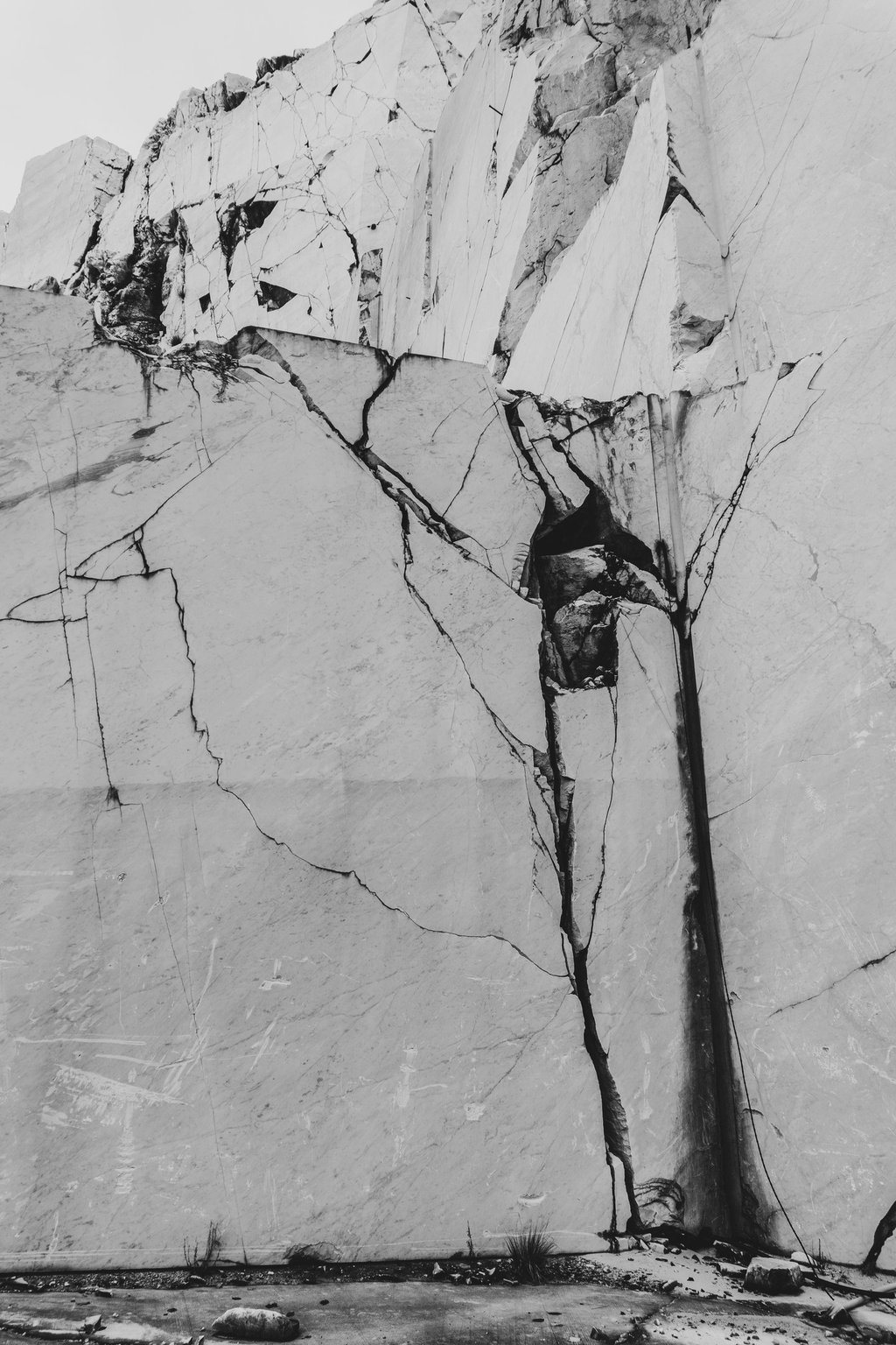 Black and white texture of a cracked white marble quarry wall with jagged stone surfaces.