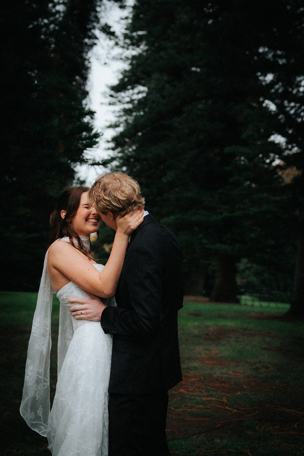 Smiling bride and groom embrace during a moody outdoor wedding photoshoot in a forest.