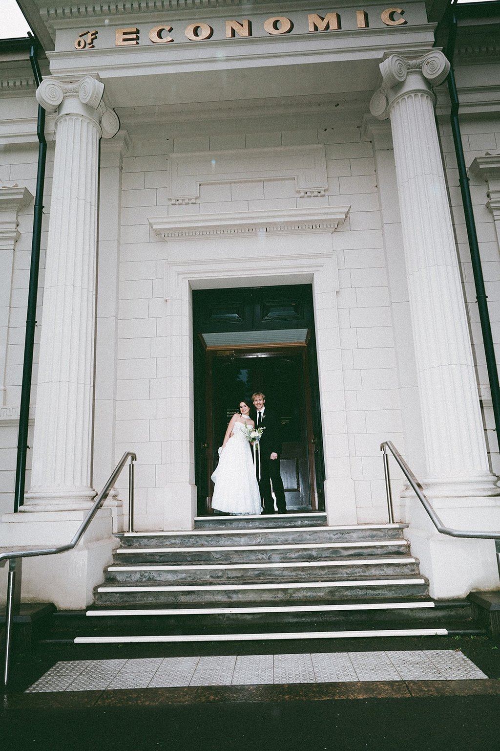 A bride and groom posing at the entrance of a historic building with large white columns.