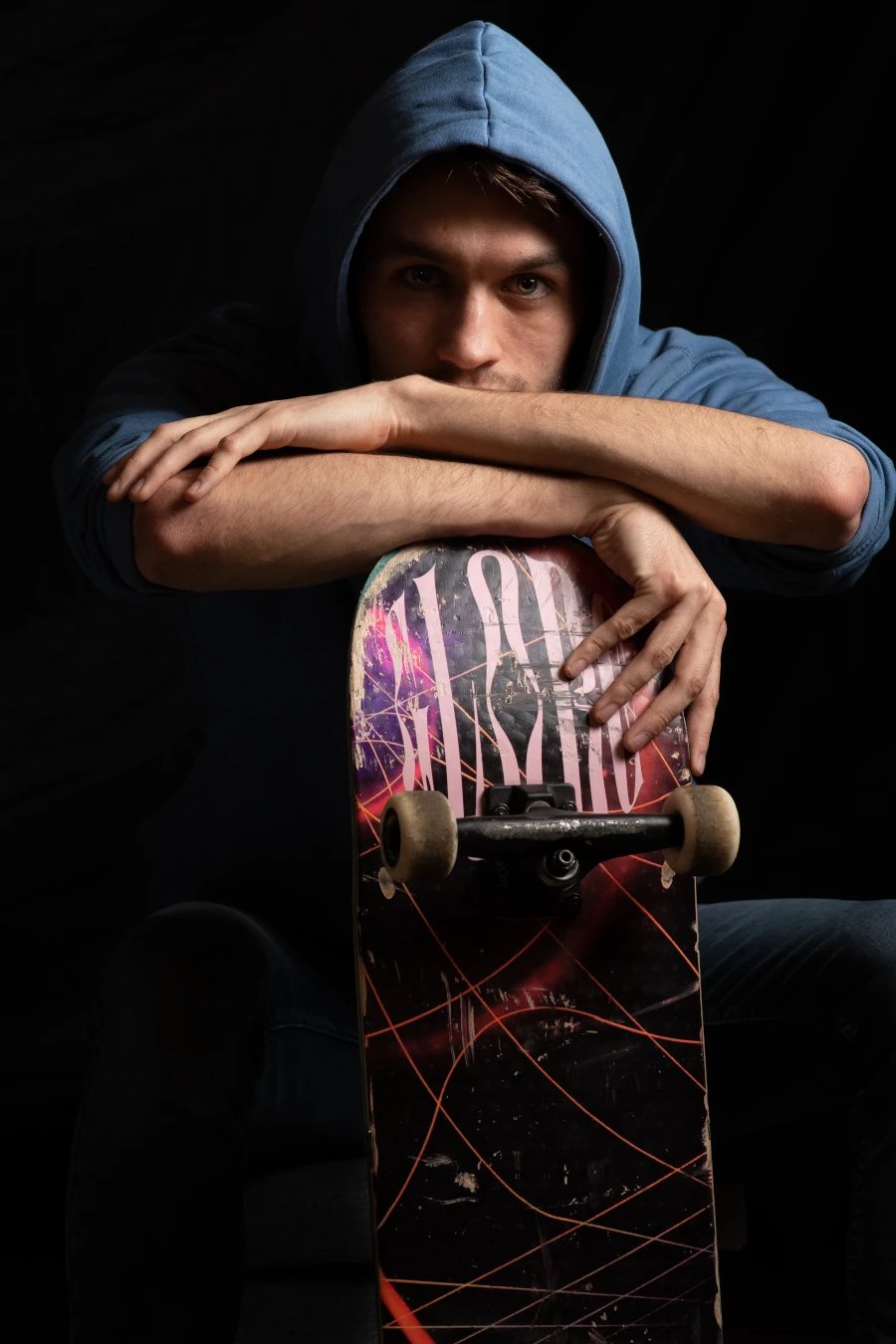 Un jeune homme vêtu d'un sweat à capuche bleu, assis avec un skateboard entre les bras