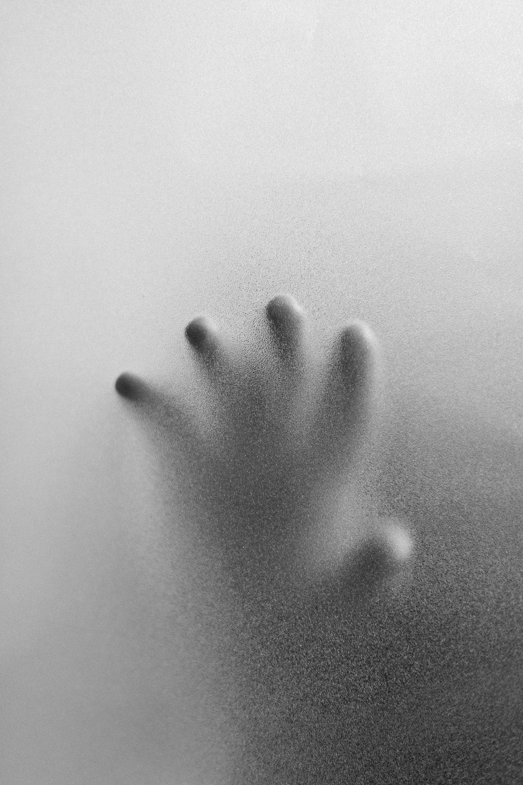 Silhouette of a hand pressed against frosted glass in a black and white artistic photography style.