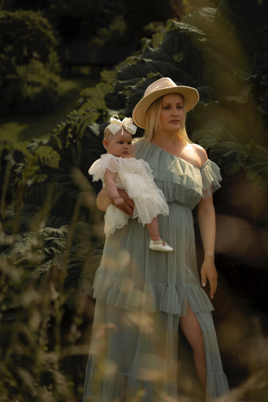 Mother in long dress and hat holding her daughter in the park 