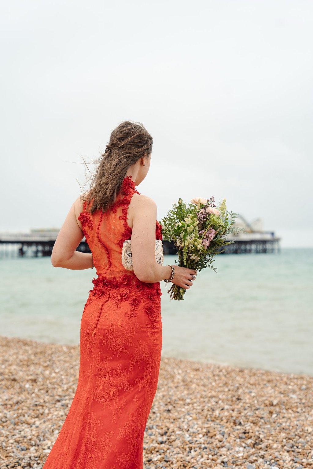 Bride in red dress standing on the beach looking at the sea