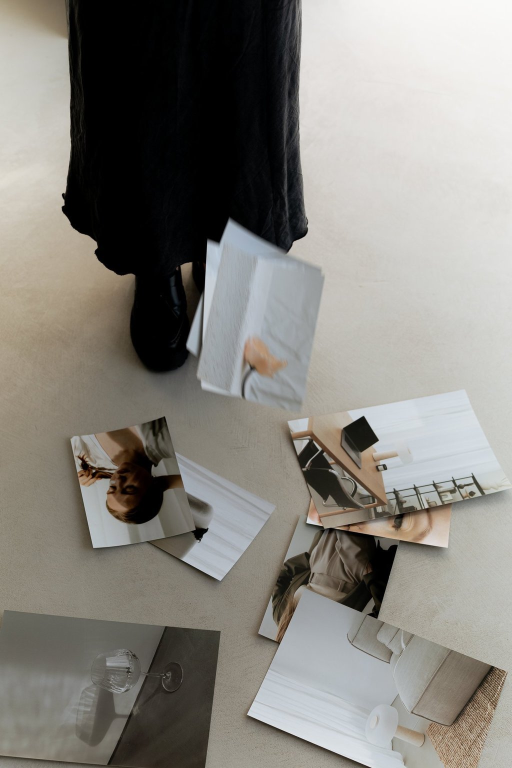A person in a black midi-skirt dropping lifestyle photos and paperwork onto a minimalist floor.