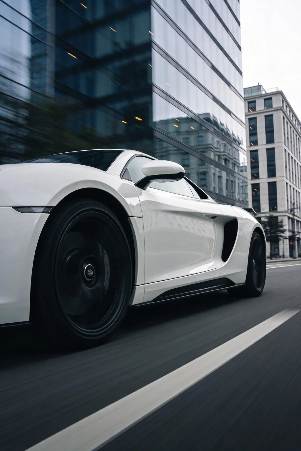 White luxury sports car driving fast on a city street past modern glass skyscrapers.