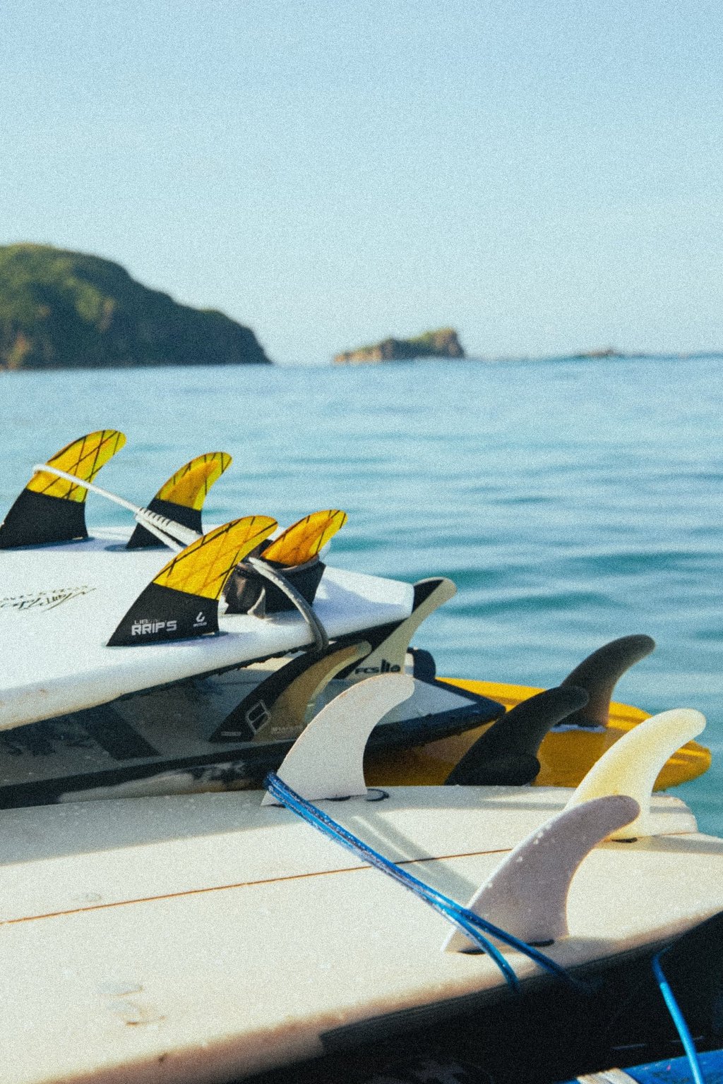 A stack of colorful surfboards with fins attached resting on a boat in the ocean.