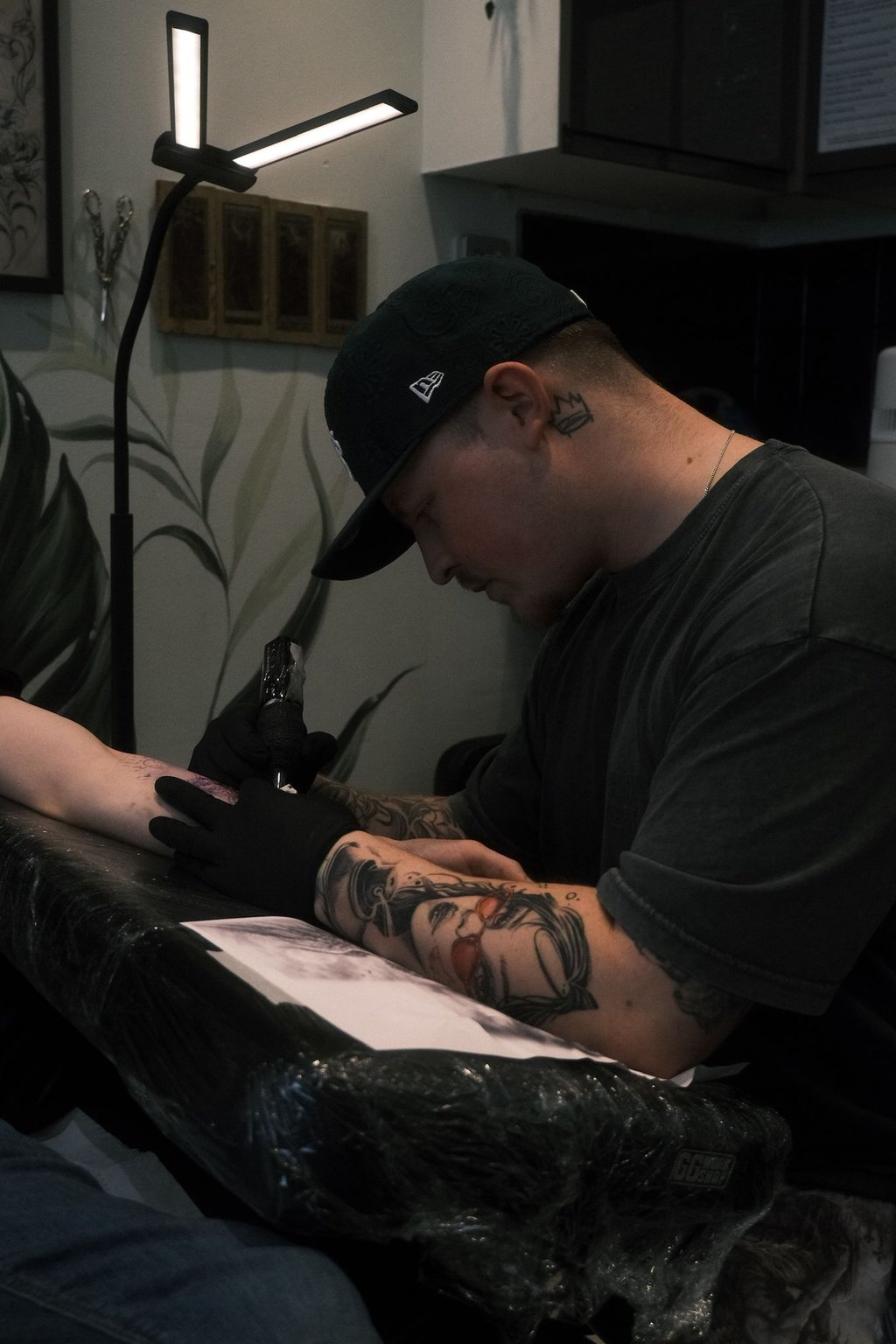 Professional tattoo artist with arm tattoos using a rotary machine to ink a client in a studio.