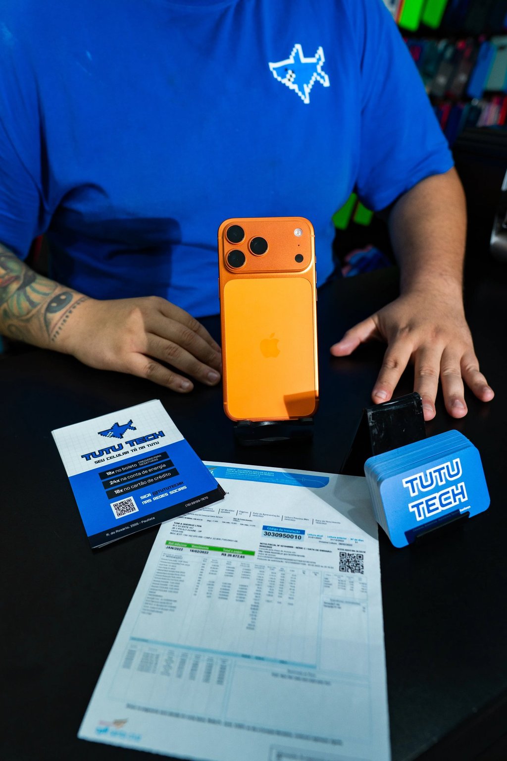 Orange iPhone smartphone on a desk with Tutu Tech branded cards and documents.