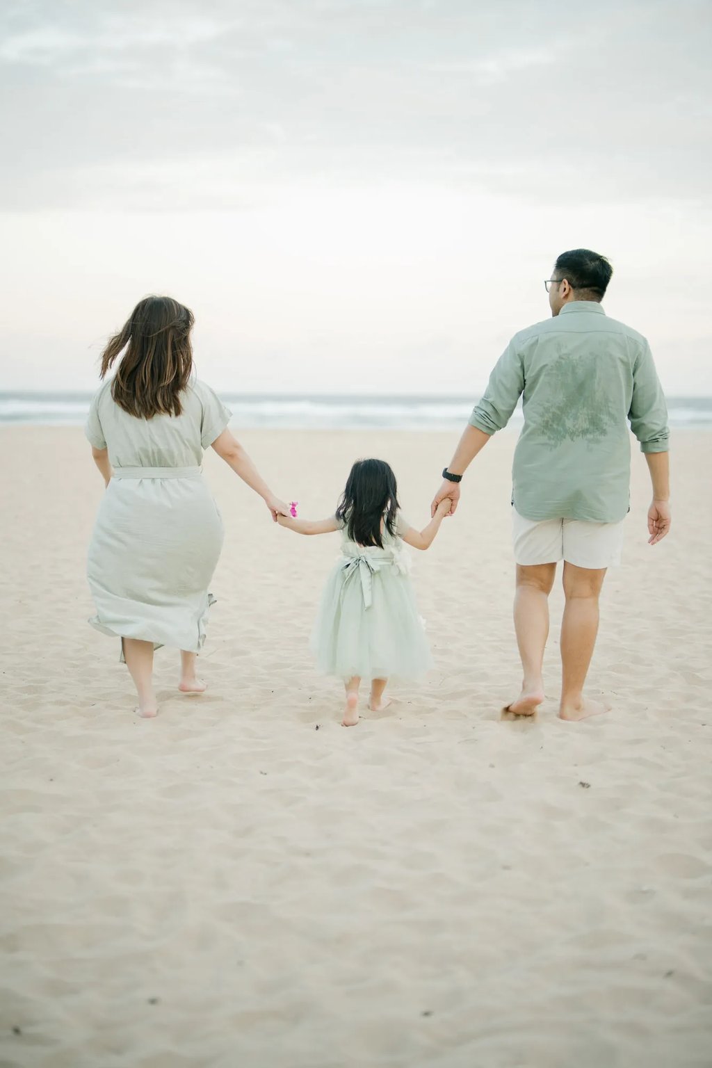 Parents and daughter walking hand in hand along the shoreline during a family photography session in Bali.