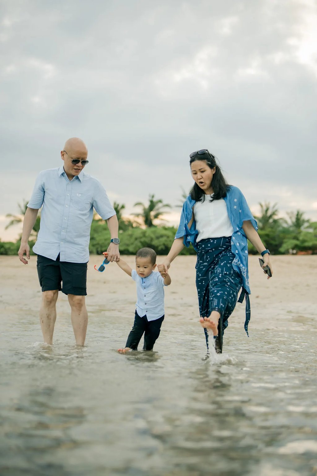 Parents walking hand in hand with their son along the shoreline during a family photography session at Nusa Dua Beach Bali