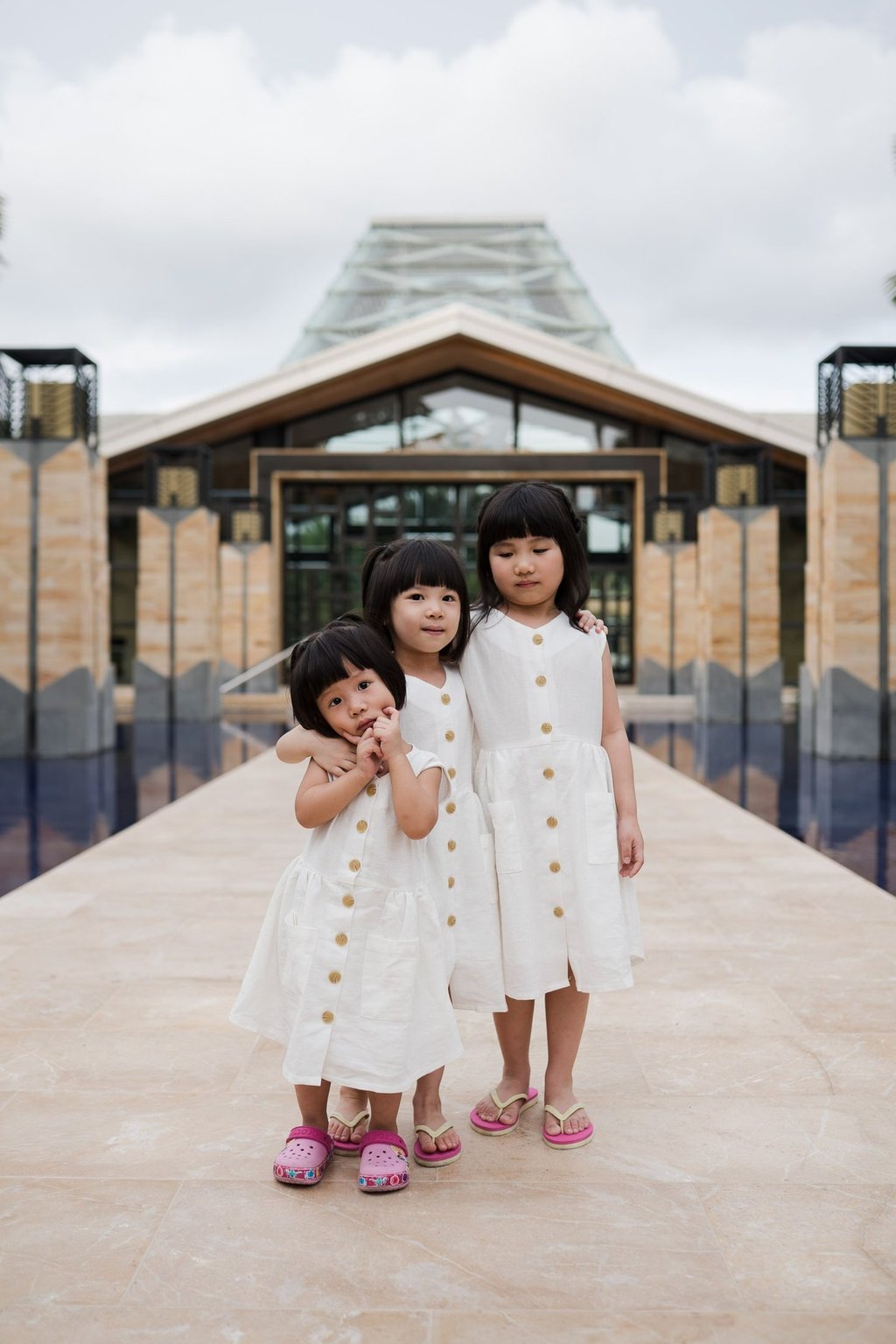 Two sisters standing together at the iconic entrance walkway of The Mulia Nusa Dua Bali during a family photo session