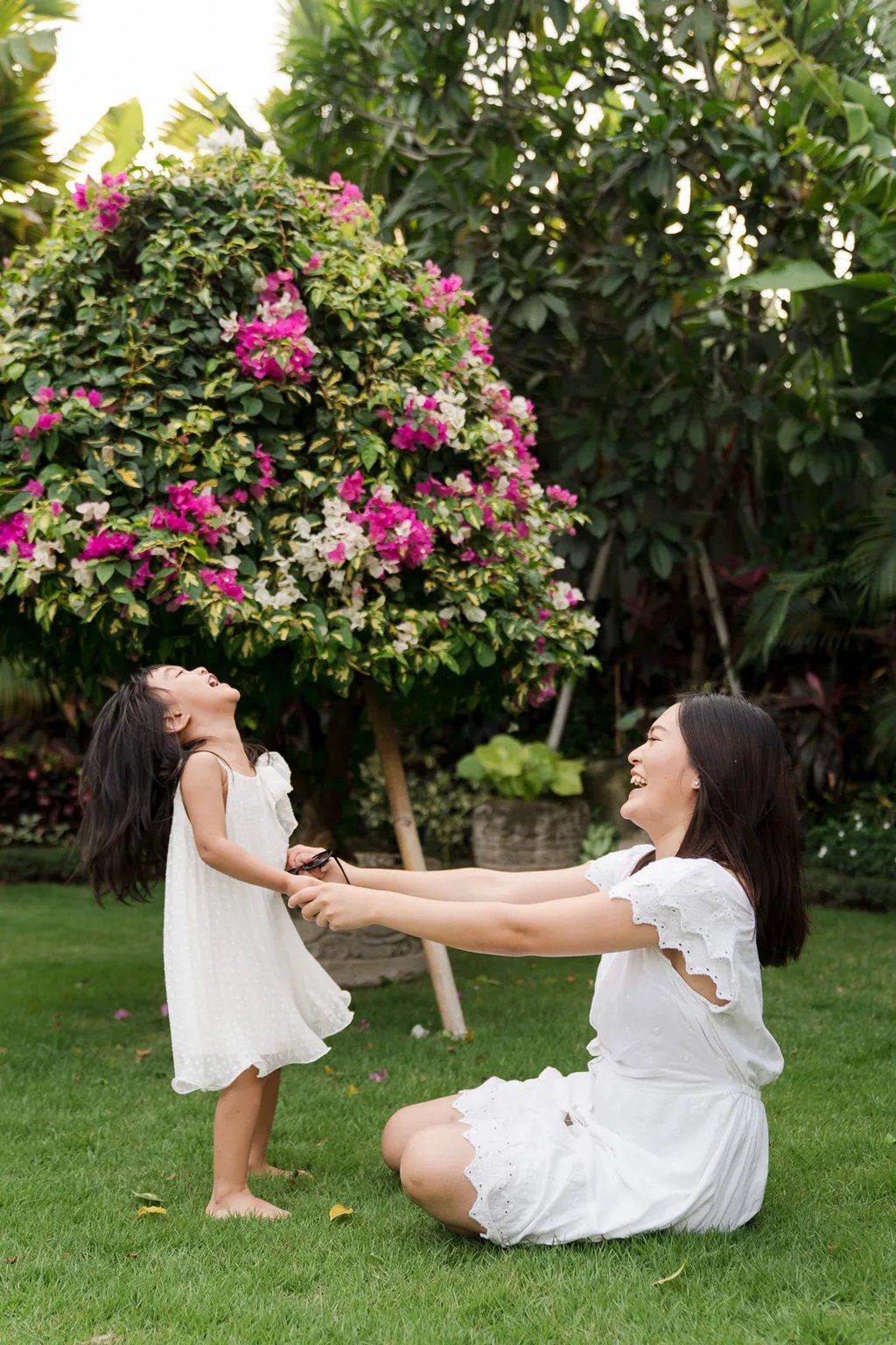 Two sisters playing together in a tropical garden during a relaxed family photography session at a private villa in Seminyak