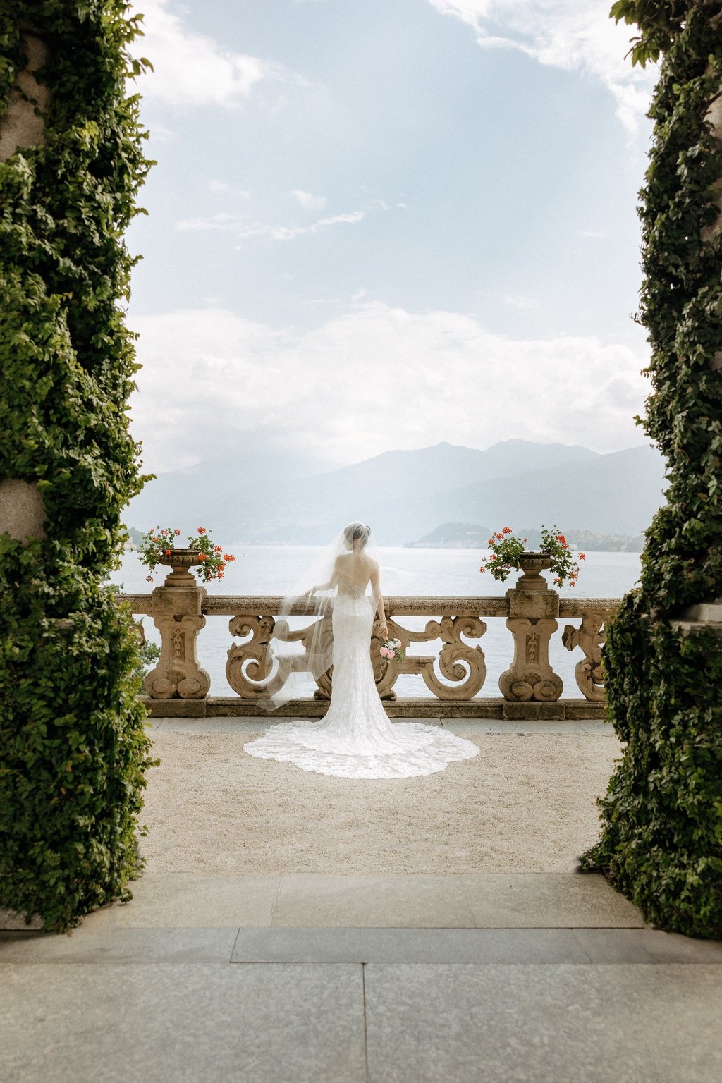 a bride in a white wedding dress standing in front of a lake at Villa Balbianello