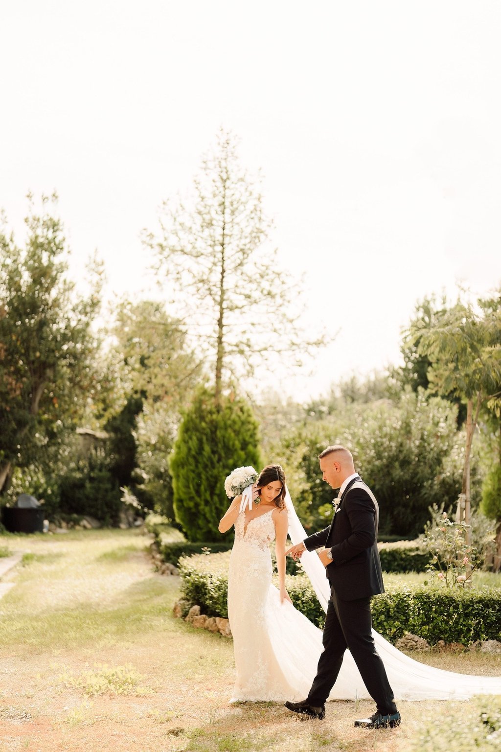 Un'elegante sposa in abito da sposa di pizzo e lo sposo in smoking nero passeggiano in un rigoglioso