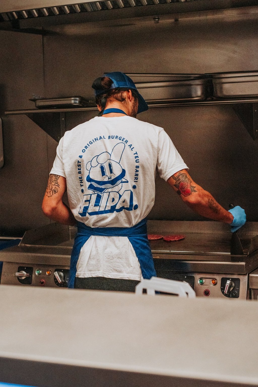 Cocinero de Flipa cocinando carne en la plancha con camiseta oficial de la marca