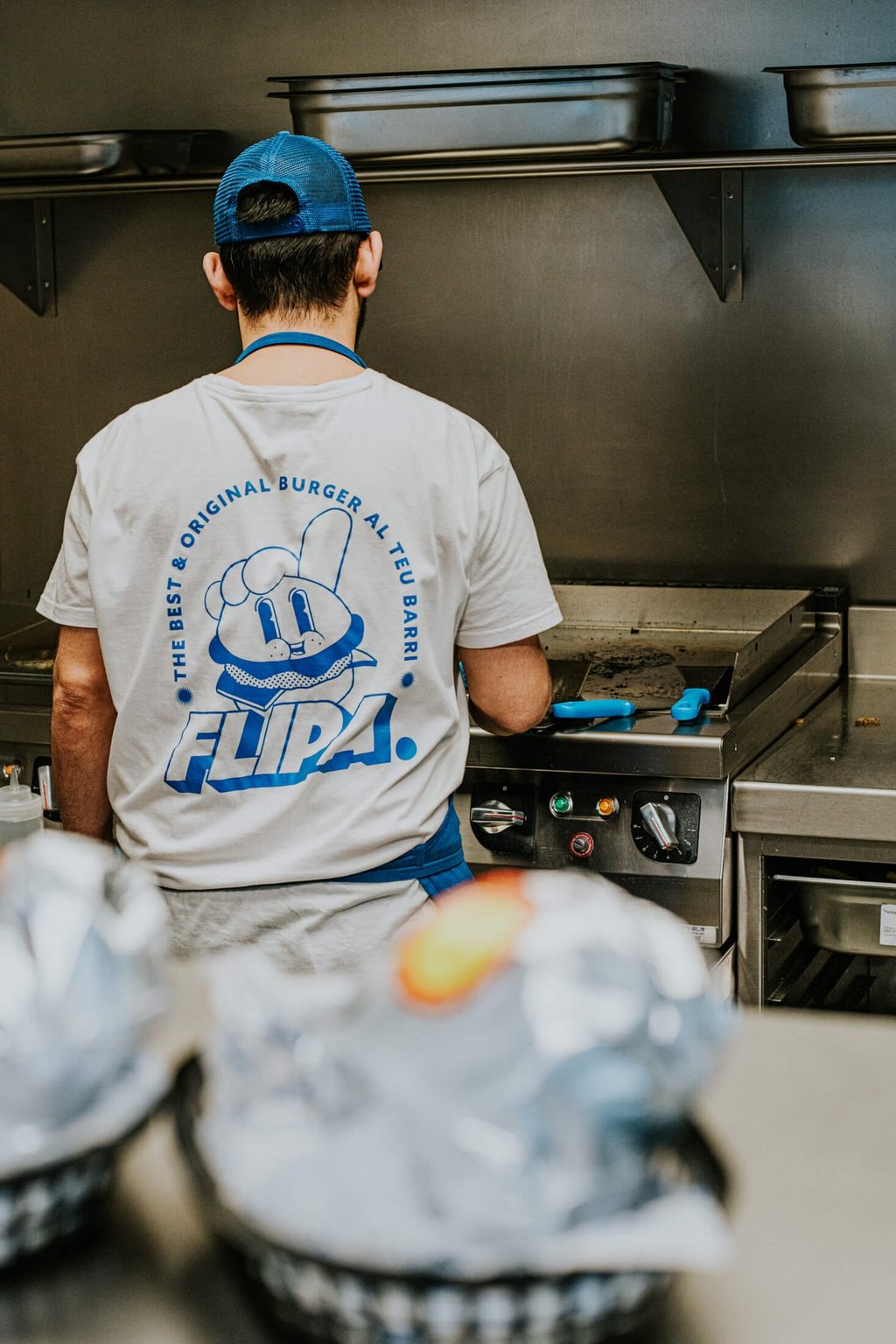 Cuiner de Flipa a la cuina amb samarreta de la marca mentre prepara burgers a la planxa