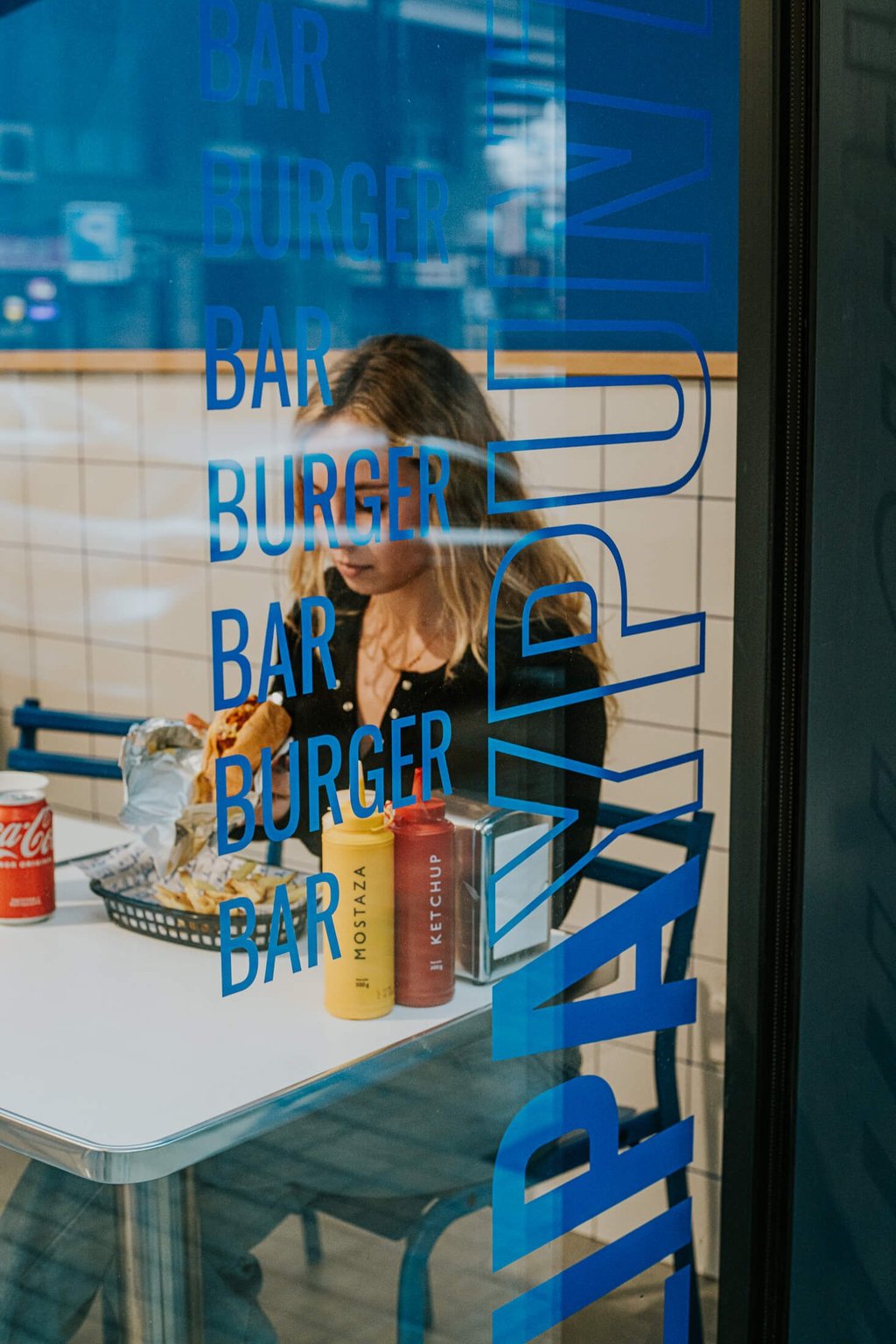 Client gaudint d’una burger a Flipa, vist a través del vidre decorat del local