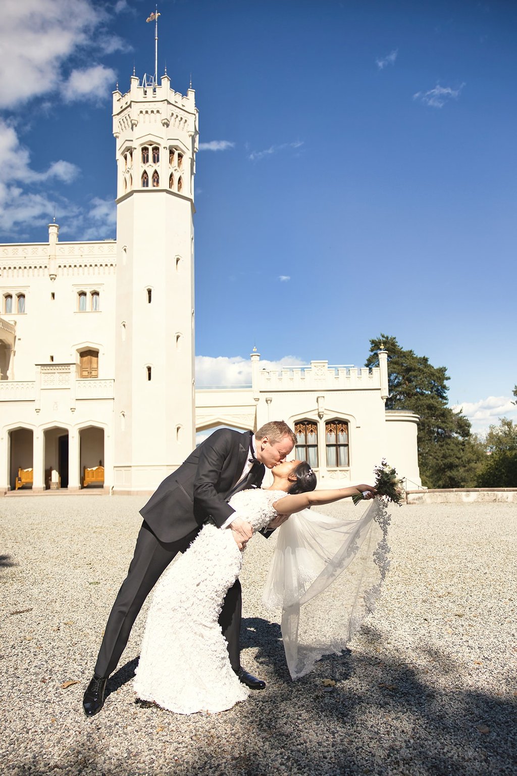En brud og brudgom som kysser foran et slott.