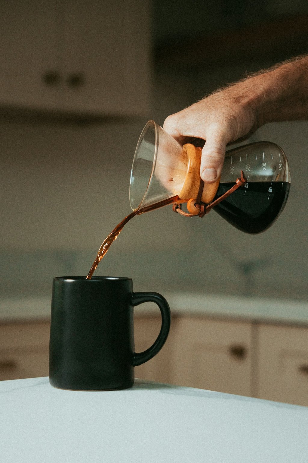 Mano sirviendo café filtrado en una taza negra usando chemex, mostrando métodos de preparación artes