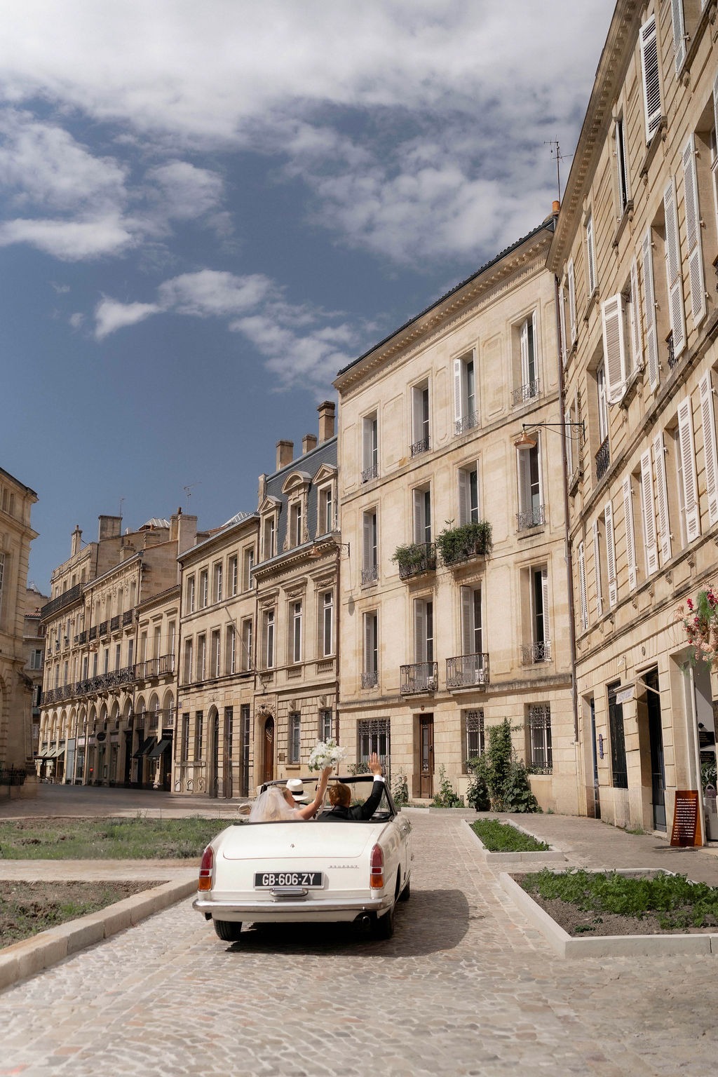 a white car driving down a cobblestone street wedding in Bordeaux