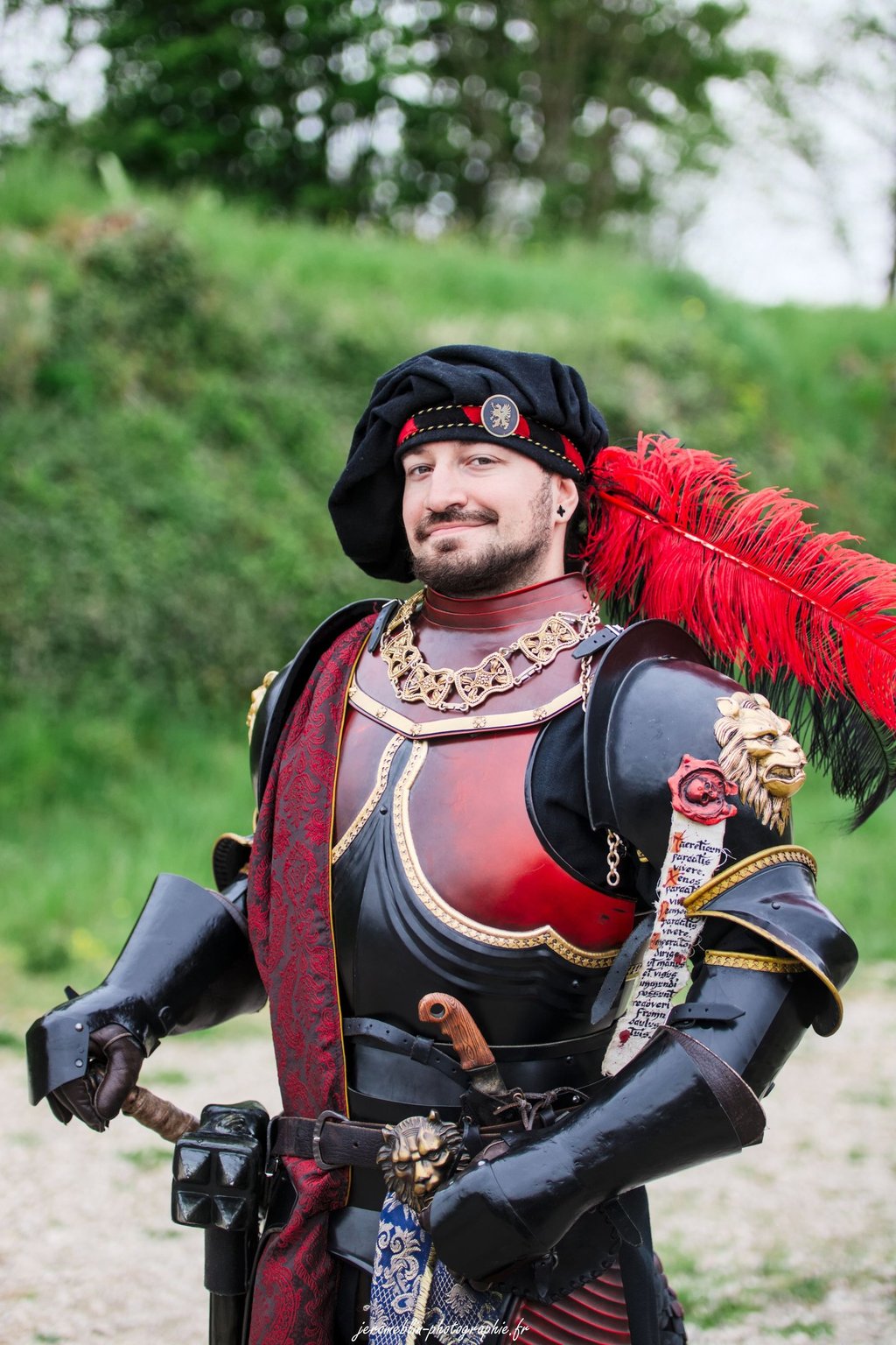 Chevalier en armure noire et rouge portant par dessus une étole en brocard