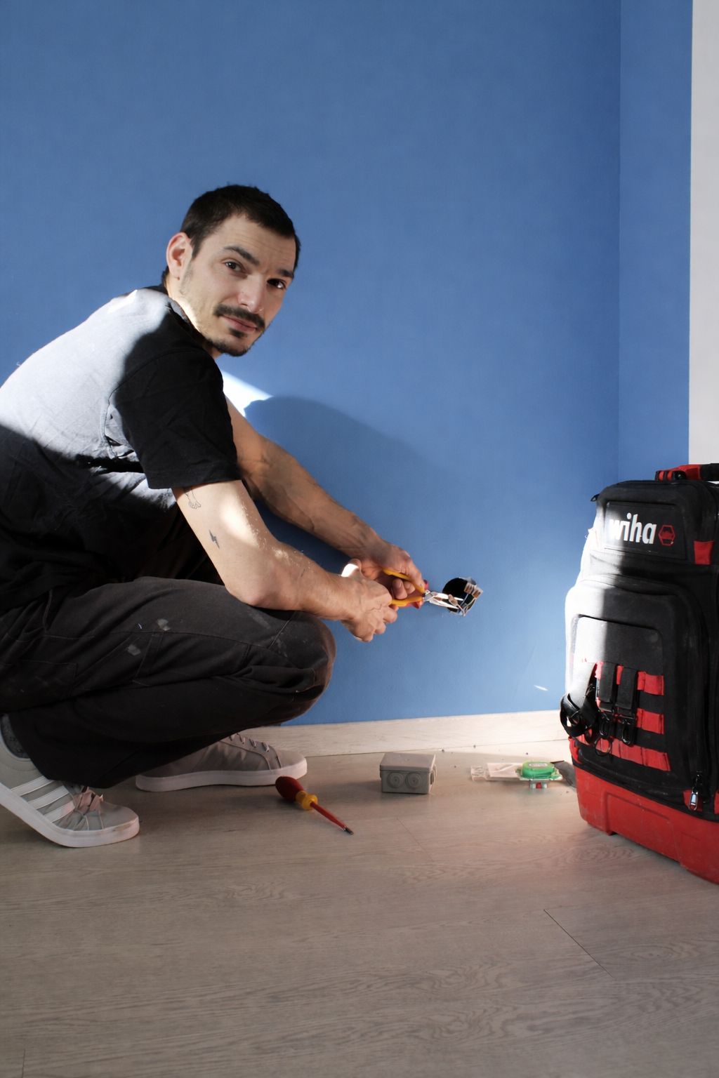 Professional electrician installing a wall socket using pliers near a Wiha tool backpack.