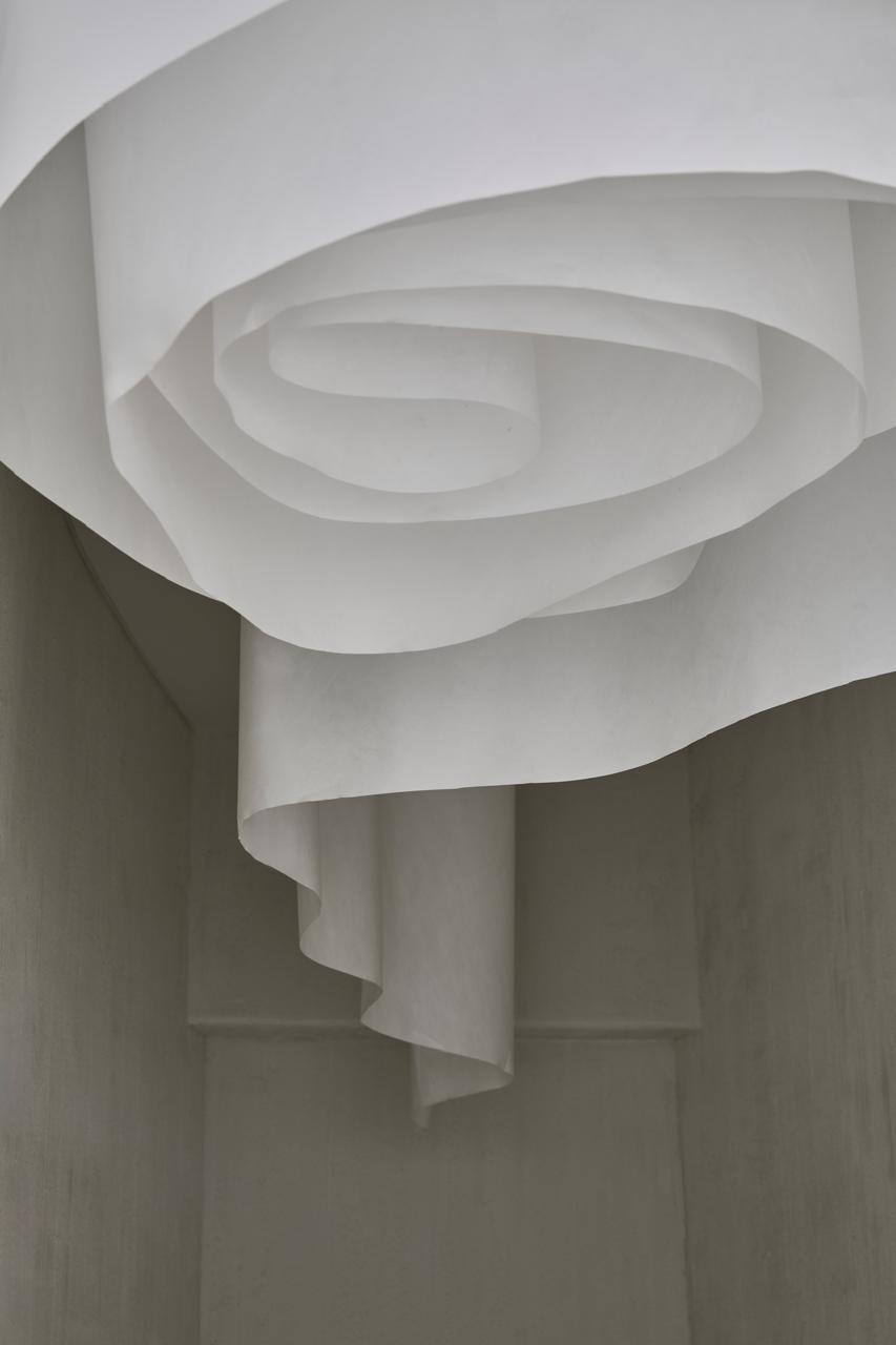 Minimalist white paper art installation with flowing spiral curves in a modern interior.
