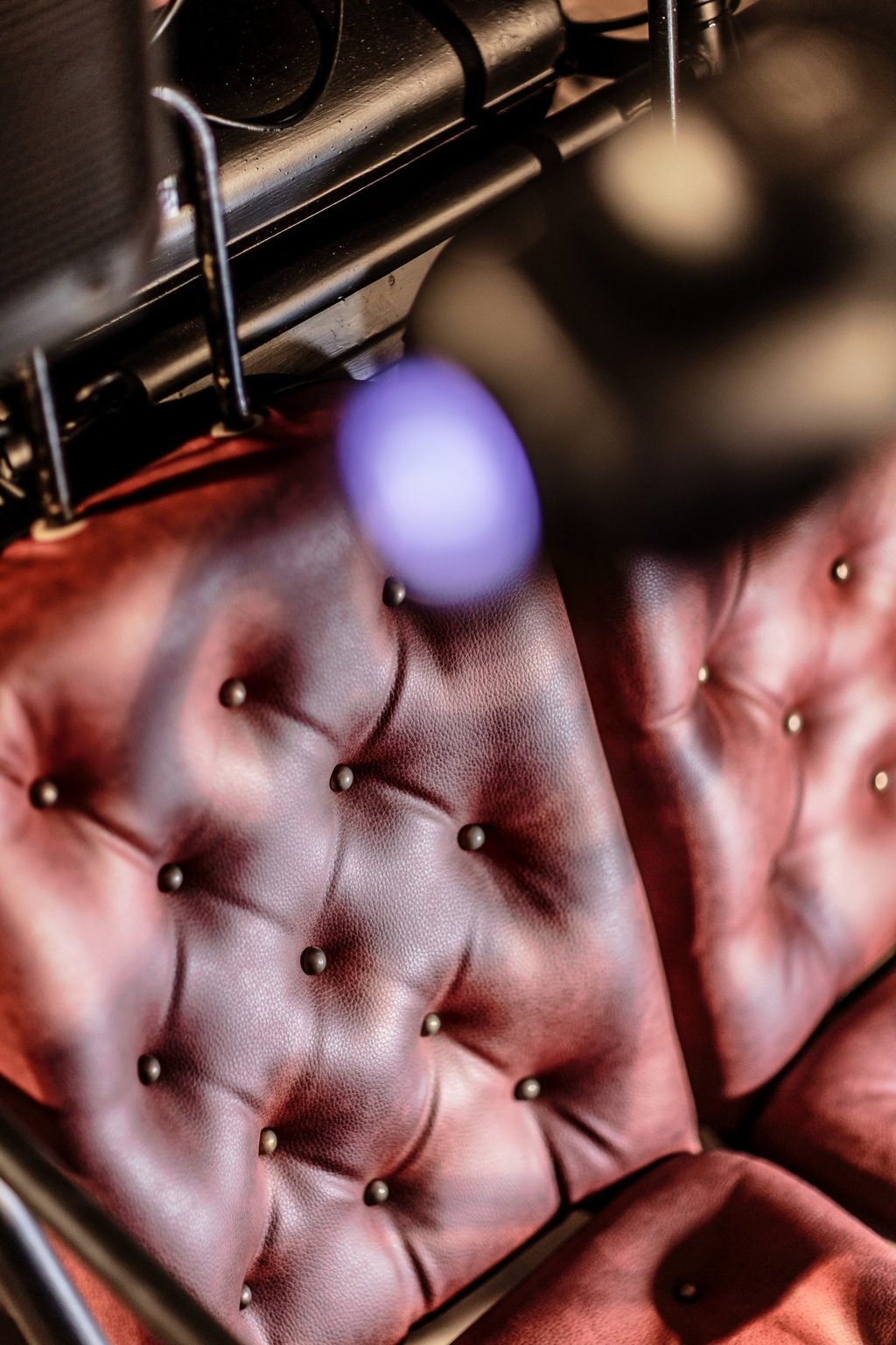 A vintage red tufted leather upholstery with decorative brass studs and soft bokeh lighting.