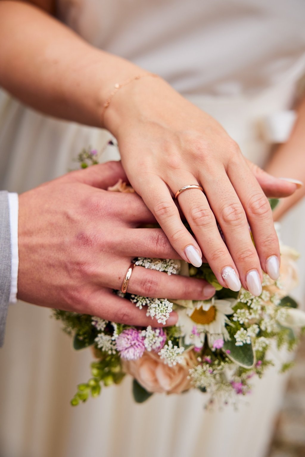 Close-up of a bride and groom's hands with gold wedding rings resting on a floral bridal bouquet.