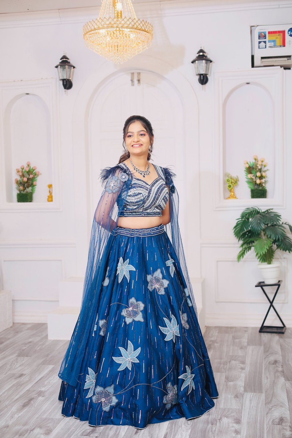 “A bride standing in a bright white studio, wearing a royal blue floral embroidered lehenga with 