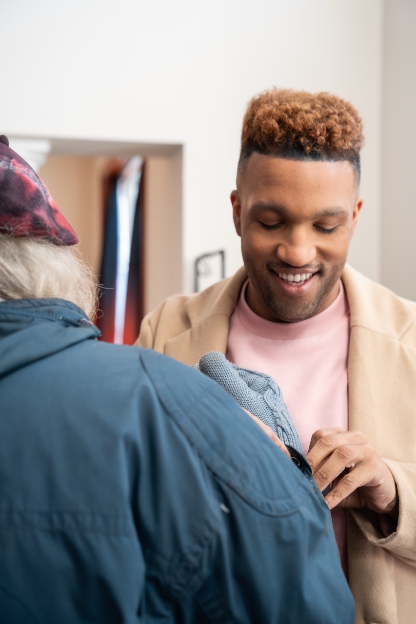 A male caregiver helps a male elderly client put on gloves