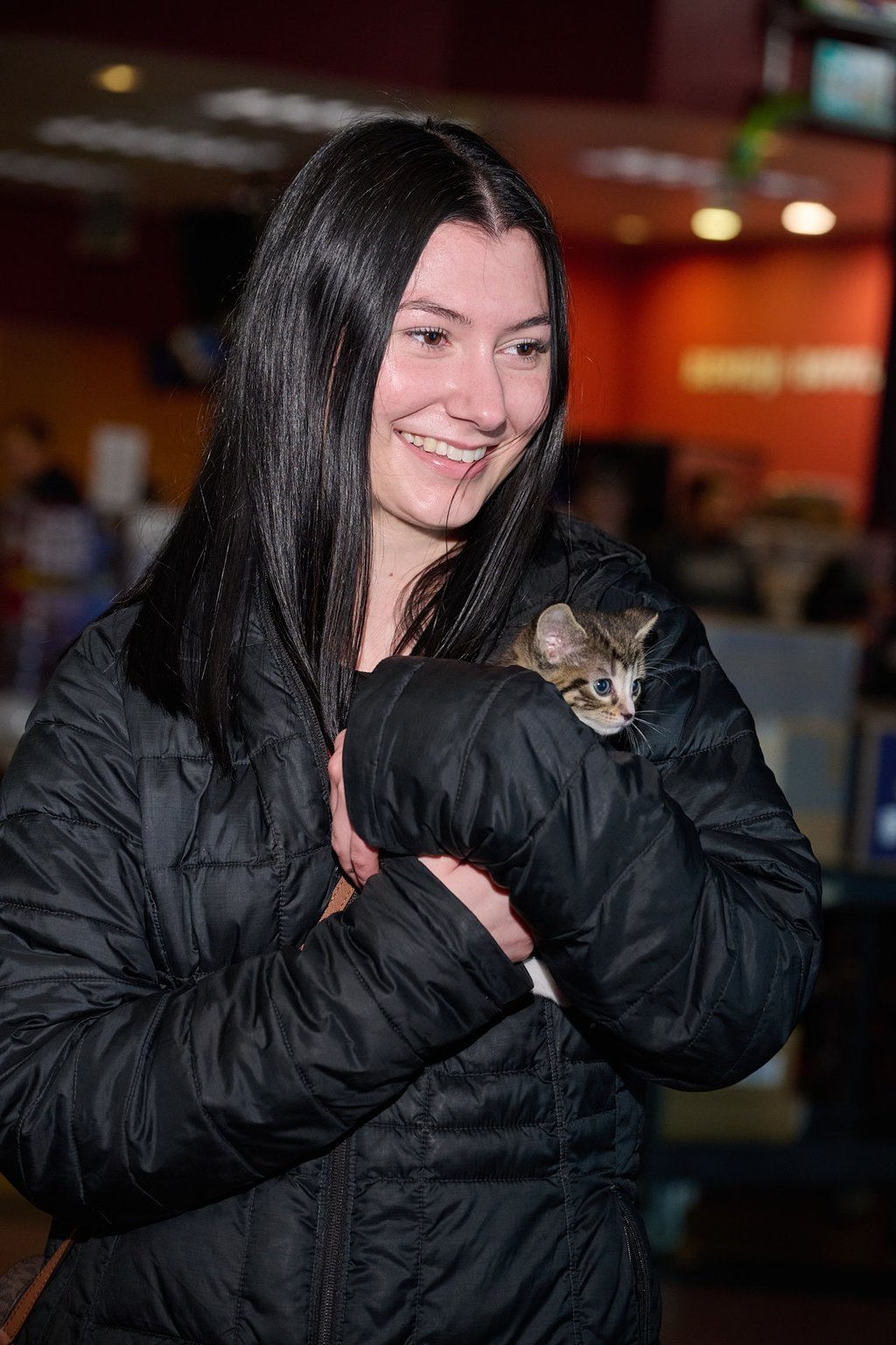 a woman in a black jacket holding a kitten looking at the same direction
